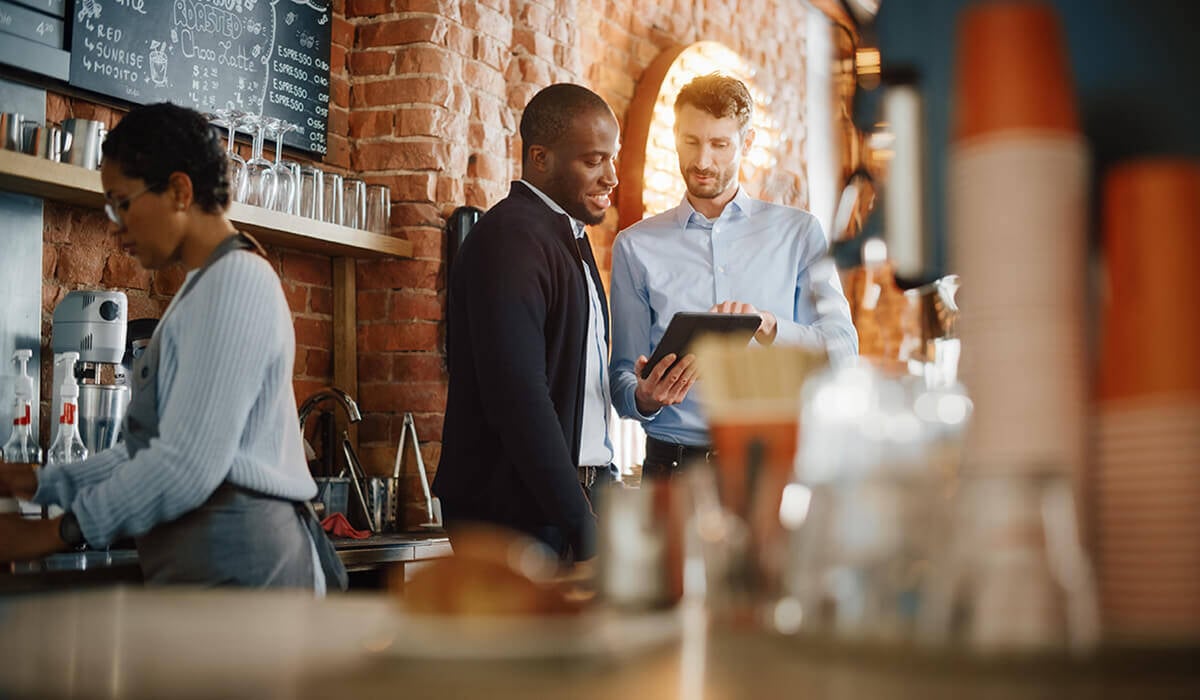 A restaurant owner looking at a tablet with another man in a suit.