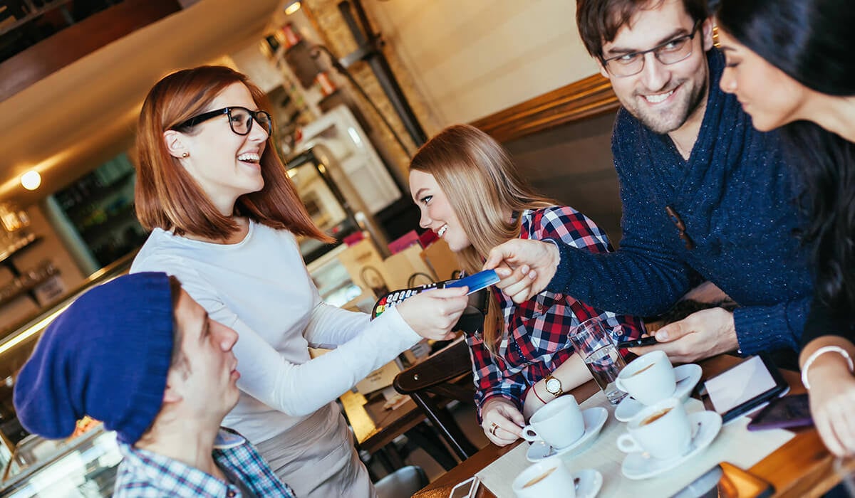 A server at a table in a restaurant taking payment on an EFTPOS Terminal