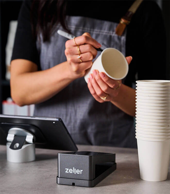 A server working at the counter in a cafe with a Zeller EFTPOS device on the counter